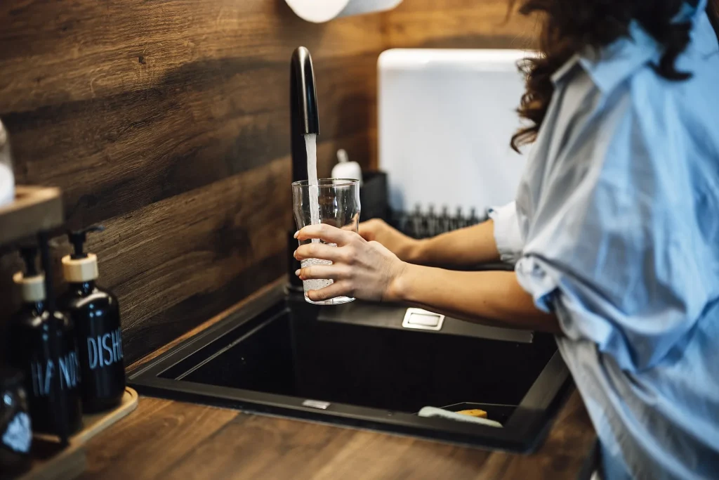 Why Your Kitchen Still Stocks Bottled Water in 2026 A person filling a glass with water at a kitchen sink - Why Your Kitchen Still Stocks Bottled Water in 2026